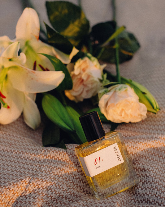 Small bottle of perfume labeled '01 Nue' with flowers on a textured surface