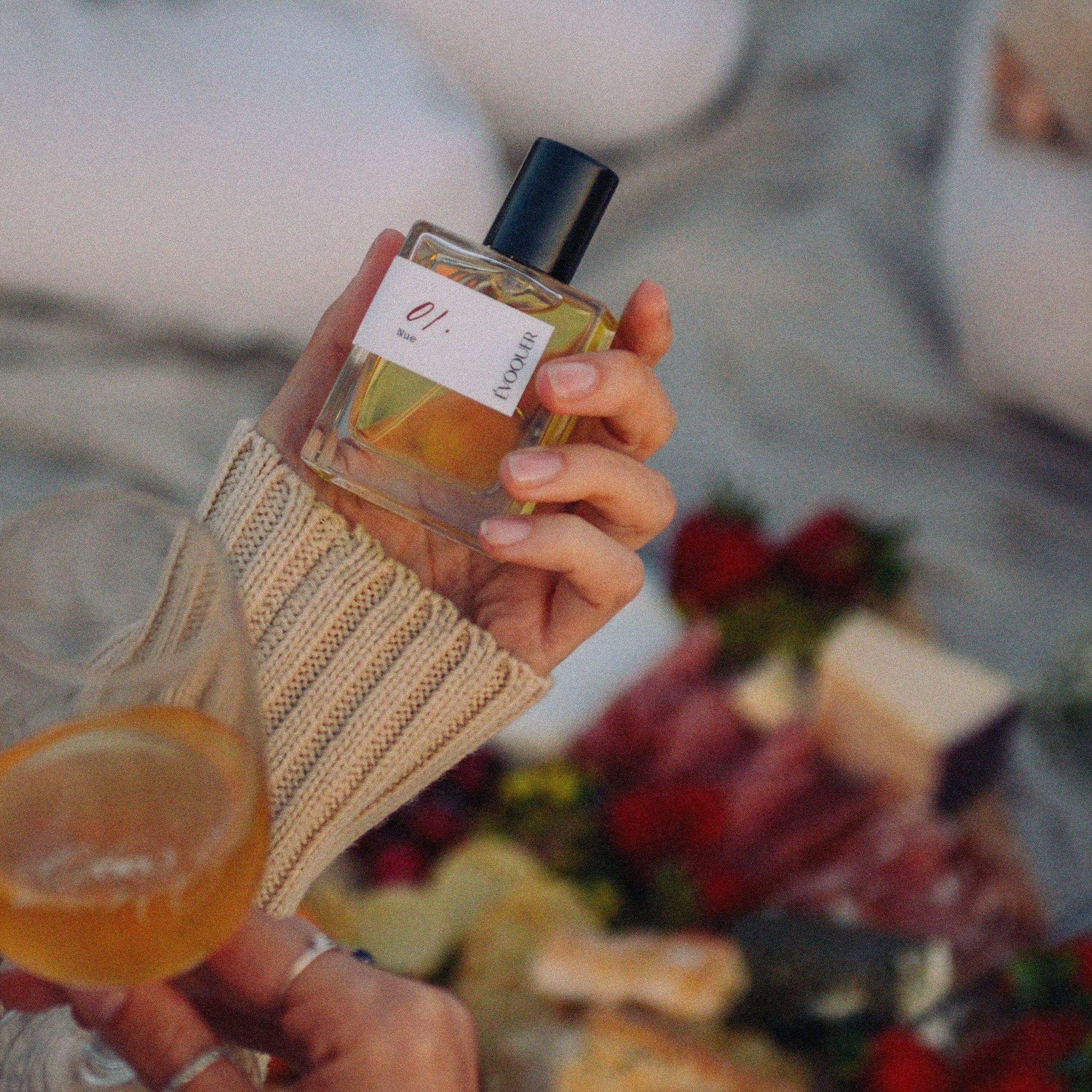 Person holding a glass of wine and perfume bottle. 